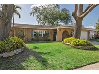 Charming home boasts a well-manicured lawn, mature trees, and an inviting, arched entryway at 8350 Monarch Cir, Seminole, FL 33772