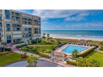 Stunning aerial view of a beachfront condo complex with a pool, palm trees, and ocean access at 1430 Gulf Blvd # 102, Clearwater Beach, FL 33767