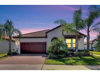 Charming single-story home featuring a brown tile roof, a spacious two-car garage, and a beautifully landscaped front yard with palm trees at 16840 Whisper Elm St, Wimauma, FL 33598