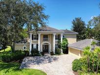 Elegant two-story home featuring grand columns, a circular driveway, and lush landscaping against a clear blue sky at 4848 Quill Ct, Palm Harbor, FL 34685