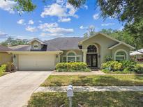 Charming home featuring lush landscaping, an attached two-car garage, and an inviting front entrance at 16608 Meadow Cove St, Tampa, FL 33624