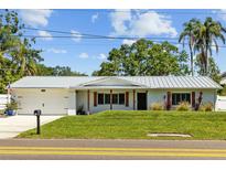 Charming single-story home with a well-manicured lawn, a metal roof, and beautiful landscaping at 1414 Sunset Ln, Lutz, FL 33549