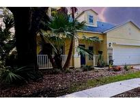 Charming yellow two-story home featuring a well-manicured lawn, palm trees, and an attached two car garage at 6230 Gannetdale Dr, Lithia, FL 33547