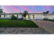 Charming home with a brick driveway, green lawn, and lush tropical landscaping under a twilight sky at 10036 40Th N St # 3, Pinellas Park, FL 33782