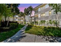 Multi-story condo with a sidewalk and tropical landscaping, including palm trees, bushes, and well-maintained grass at 2650 Countryside Blvd # C203, Clearwater, FL 33761