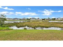 A serene pond view surrounded by lush greenery, with houses in the background under a partly cloudy sky at 10936 Rainbow Pyrite Dr, Wimauma, FL 33598