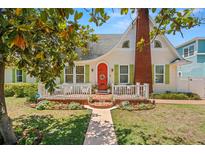 Charming home showcasing a well-manicured lawn, red brick chimney and quaint, orange front door with green shutters at 1603 S Arrawana Ave, Tampa, FL 33629