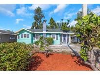 Charming, one-story home featuring a bright, turquoise exterior, manicured landscaping, and a unique chimney design at 2016 Douglas Ave, Clearwater, FL 33755