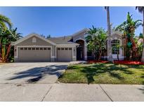 Charming home with a three car garage and tropical landscaping with nice curb appeal under a clear, blue sky at 476 Denise St, Tarpon Springs, FL 34689