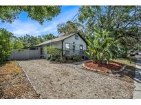 Charming home featuring tropical landscaping, a small front porch, and a well-maintained, light gray picket fence at 7309 N Huntley Ave, Tampa, FL 33604