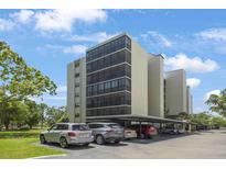 Low-angle view of a multi-story condo building with covered parking beneath it in front of lush, green trees at 2900 Cove Cay Dr # 1B, Clearwater, FL 33760