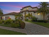 Stately two-story stucco home with a tile roof, arched entryway, lush landscaping, and a paver driveway at 949 Symphony Isles Blvd, Apollo Beach, FL 33572