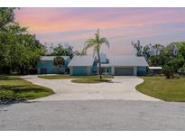 Charming light-blue home with a circular driveway, mature palm tree, and ample parking at 1305 Greenfield Cir, Venice, FL 34292
