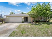 Charming single-story home featuring a two-car garage, arched entryway, and mature landscaping under a sunny sky at 5263 Kirkwood Ave, Spring Hill, FL 34608
