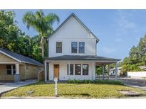 Charming two-story home with a covered front porch, a manicured lawn, and a bright exterior paint at 1230 E Emma St, Tampa, FL 33603