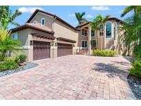 A luxurious home boasting a paver driveway, three-car garage, and lush tropical landscaping at 6315 Marbella Blvd, Apollo Beach, FL 33572