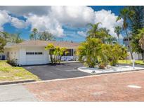 Charming single-story home with lush tropical landscaping, a brick-paved street, and an attached one-car garage at 225 Cevera Dr, Dunedin, FL 34698