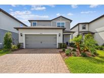 Charming two-story home featuring a gray exterior, brick driveway, and manicured landscaping at 17652 Ramble On Way, Land O Lakes, FL 34638