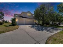 Charming two-story home with a spacious driveway and a three-car garage, surrounded by mature trees under a dusk sky at 13421 Sydney Rd, Valrico, FL 33594