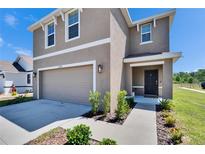 Two story home features a two car garage, neutral stucco facade, manicured lawn, and covered front porch at 16894 Delia St, Wimauma, FL 33598