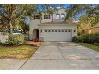 Two-story home with a two-car garage, well-manicured lawn, and mature trees providing shade at 2436 Spring Hollow Loop, Wesley Chapel, FL 33544