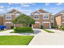 Inviting two-story townhome featuring a two-car garage, manicured lawn, and lush shrubbery at 10135 Post Harvest Dr, Riverview, FL 33578