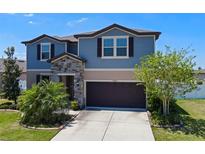Charming two-story home with blue siding, stone accents, a dark garage door and landscaped yard at 13871 Carlow Park Dr, Riverview, FL 33579