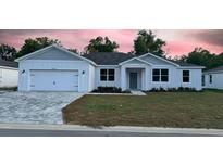 Charming single-story home featuring a well-manicured lawn and a brick-paved driveway and a modern, white facade at 37565 Teri Ct, Dade City, FL 33525