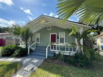 Charming home featuring light green exterior paint, red door, palm trees, and inviting front porch at 1211 E Curtis St, Tampa, FL 33603