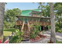 Two-story green house with multiple decks, surrounded by lush greenery and mature trees at 8614 Hibiscus Dr, Tampa, FL 33637
