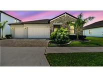 Beautiful single-story home featuring stone accents, a two-car garage, manicured landscaping, and a brick paved driveway at 21506 Snowy Orchid Ter, Land O Lakes, FL 34637