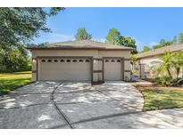 Beige two-car garage with a wide driveway and decorative doors, located in a sunny, landscaped neighborhood at 7519 Berna Ln, Land O Lakes, FL 34637