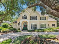 Stately two-story home featuring a lush front yard, mature trees, and an arched entrance with a green front door at 1927 Curry Rd, Lutz, FL 33549