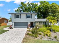Well-maintained two-story home with a paved driveway, lush landscaping, and a gray garage door at 2525 Madrid S Way, St Petersburg, FL 33712