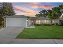 Charming single-story home featuring a two-car garage, stone accents, and a well-maintained lawn with a twilight sky background at 4148 102Nd N Pl, Clearwater, FL 33762