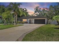 Charming single-story home featuring a long driveway, lush landscaping, and a two-car garage at sunset at 6821 Date Palm S Ave, St Petersburg, FL 33707