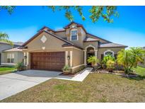 Inviting exterior with a two-car garage, arched entryway, fresh landscaping, and a well-manicured lawn at 8103 Tar Hollow Dr, Gibsonton, FL 33534