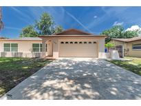 Beige one-story home showcasing a two-car garage and a well-maintained lawn under a partly cloudy sky at 11210 Wheeling Dr, Tampa, FL 33625