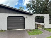 Attached garage with a brown door, textured white exterior walls, and an arched entryway with an iron gate to the front entry at 1309 Malone Ave, Spring Hill, FL 34606