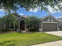Charming single-story home with a well-manicured lawn and beautiful palm trees under a partially cloudy sky at 2603 Valencia Grove Dr, Valrico, FL 33596
