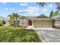Charming single-story home features a manicured lawn, two-car garage, and vibrant red front door at 1077 Captains Way, Tarpon Springs, FL 34689
