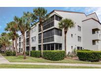 Condo building featuring a clean white facade, screened balconies, and lush tropical landscaping at 2593 Countryside Blvd # 7204, Clearwater, FL 33761