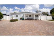 Charming single-story home with a large brick driveway, manicured landscaping, and quaint front porch seating at 2805 W Patterson St, Tampa, FL 33614