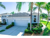 Light blue home featuring a three-car garage, well-manicured bushes, and elegant palm tree landscaping at 1257 Lyndhurst Greens Dr, Sun City Center, FL 33573