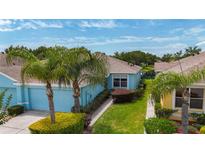 Charming blue home featuring a two-car garage, lush landscaping, and picturesque palm trees in a well-maintained community at 11457 Captiva Kay Dr, Riverview, FL 33569