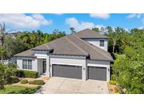 Beautifully landscaped, two-story home featuring a three car garage and manicured lawn with lush trees in the background at 7207 Peregrina Loop, Wesley Chapel, FL 33545