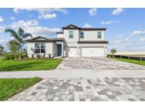 Two-story home featuring a 3 car garage, brick paver driveway, and a blue front door at 13631 Sunlight Meadow Dr, Riverview, FL 33578