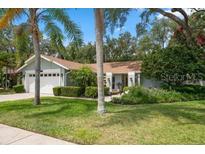 Charming single-story home featuring a well-manicured lawn, mature trees, and an attached two-car garage at 4765 Lake Valencia W Blvd, Palm Harbor, FL 34684