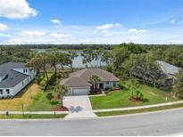 Beautiful single-story home with a well-manicured lawn, mature trees, and a scenic lake view in the background at 15615 Serengeti Blvd, Spring Hill, FL 34610