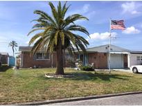 Charming brick home featuring a lush front lawn, vibrant palm tree, and an American flag displayed proudly at 3850 Sablewood Dr, Holiday, FL 34691